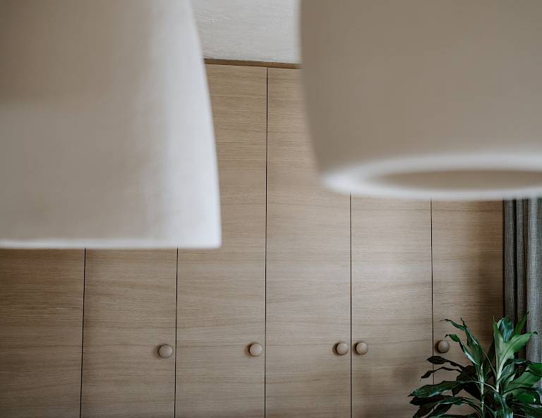 Due lampade sospese davanti a un armadio di legno vicino a una pianta. Design minimalista e moderno.