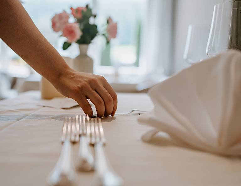 Mano sistema posate su tavolo in elegante ristorante, sullo sfondo vaso con rose.