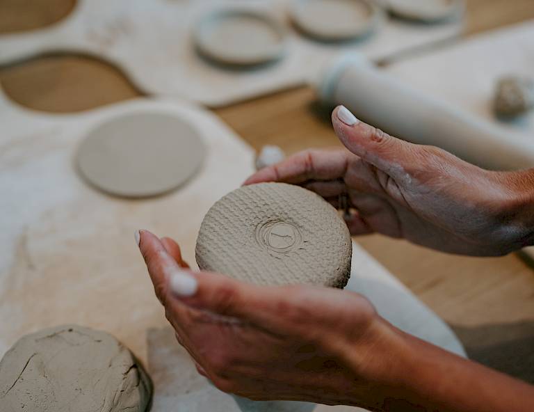 Mani modellano un disco di argilla su un tavolo, con strumenti di ceramica sullo sfondo.