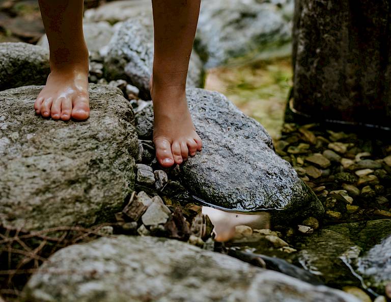 Persona a piedi nudi in equilibrio su rocce in un ruscello nel bosco.