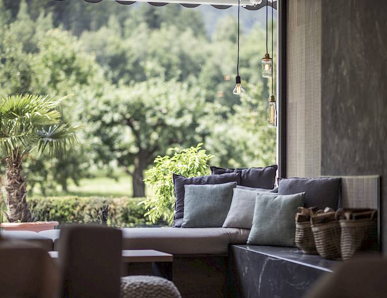 Interno accogliente con vista su paesaggio verde e alberi attraverso una grande finestra aperta.