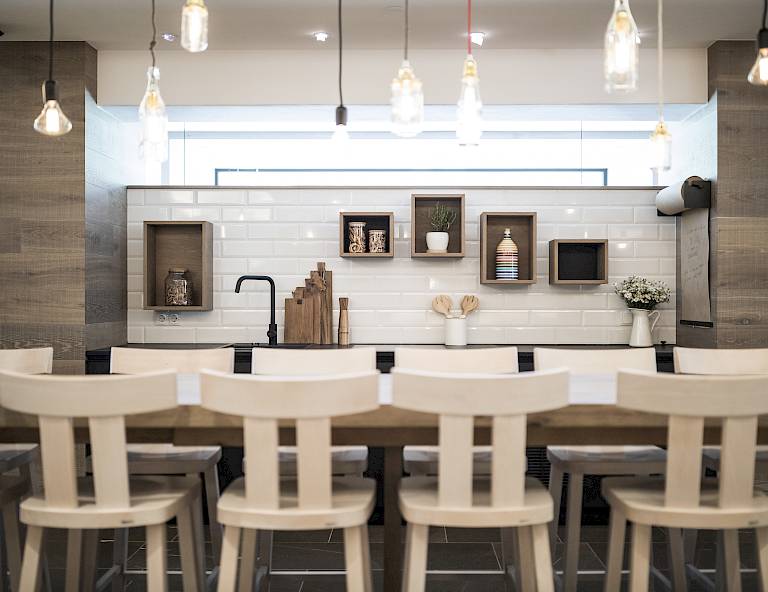 Cucina moderna con sedie bianche, lampade sospese e decorazione minimalista su mensole in legno.