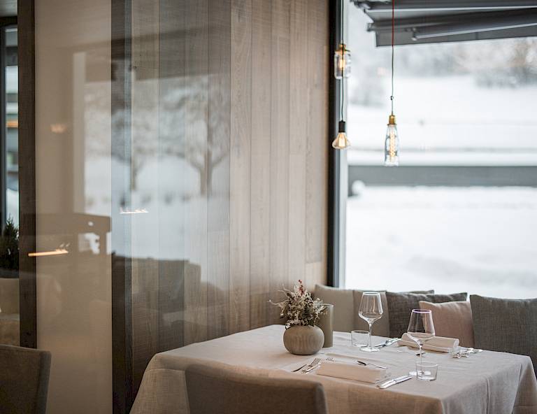 Interni eleganti di un ristorante con tavolo apparecchiato, vista su paesaggio innevato dalla finestra.