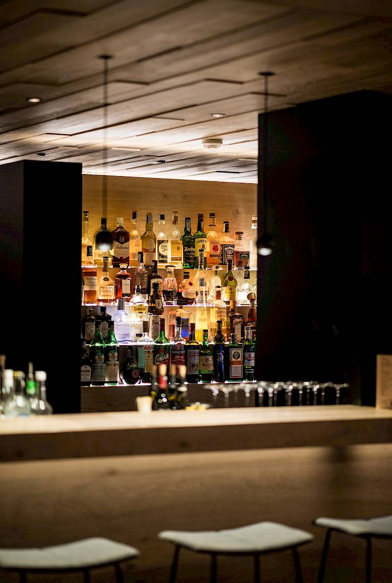 Bar con decorazioni in legno elegante, bottiglie sugli scaffali e illuminazione soffusa.