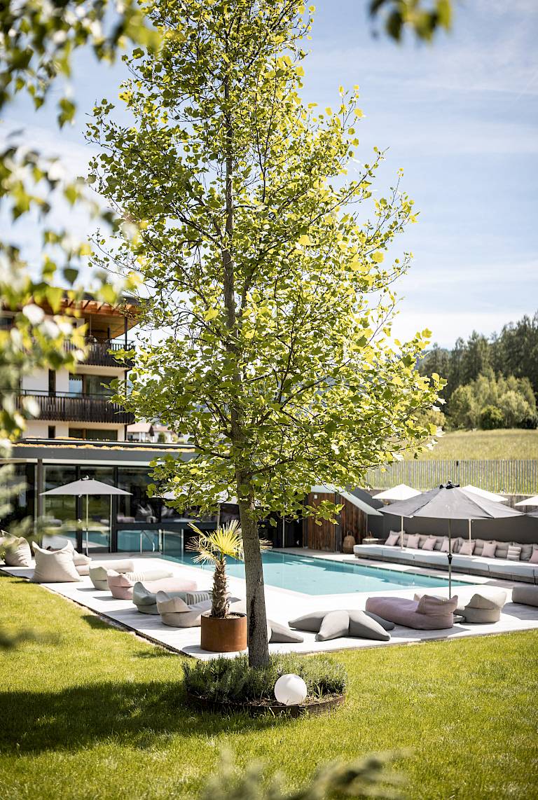 Giardino di lusso con piscina, lettini moderni e ombrelloni sotto un cielo blu splendente.