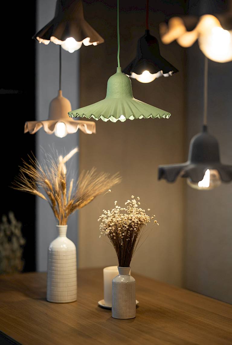 Lampade a sospensione in ceramica illuminano vasi con fiori secchi su un tavolo in un ambiente accogliente.