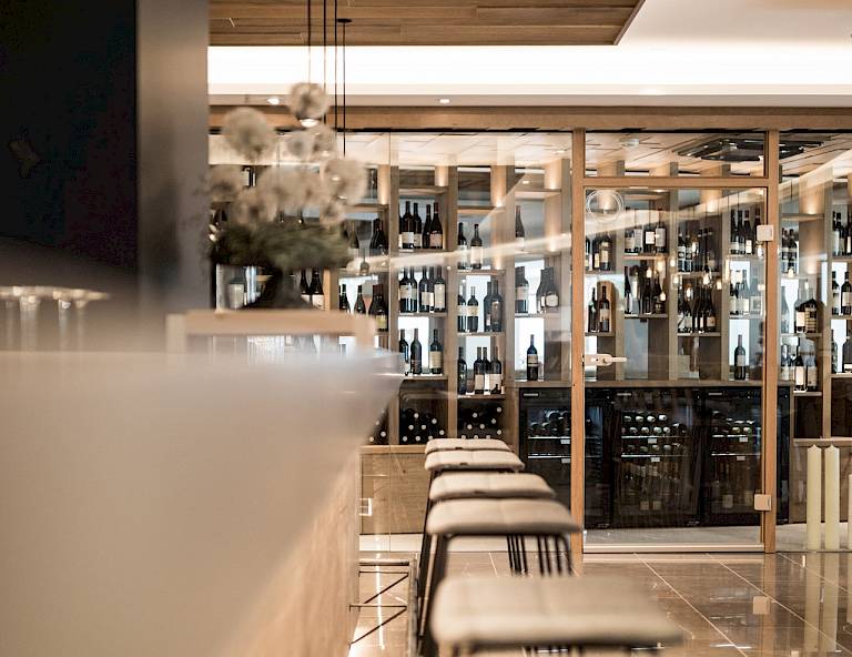 Enoteca moderna con scaffali in legno pieni di bottiglie, interni eleganti con sgabelli e luce soffusa.