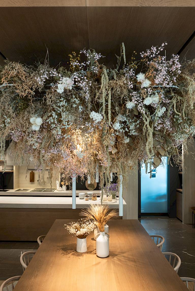 Un grande tavolo di legno in una cucina moderna, ornato con fiori secchi sospesi e vasi.