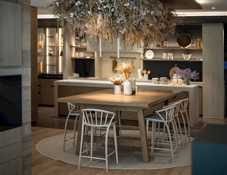 Sala da pranzo moderna con tavolo in legno e sedie bianche, decorata con lampade sospese e fiori secchi.