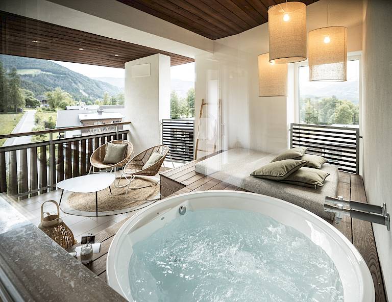 Vasca idromassaggio interna con vista panoramica sulle montagne, soffitto in legno, lampade e sedie lounge.