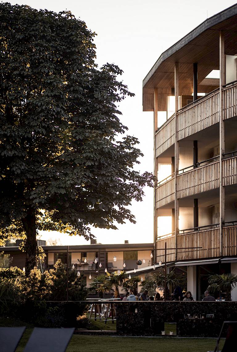 Edificio a più piani con giardino circostante al tramonto, albero in primo piano.