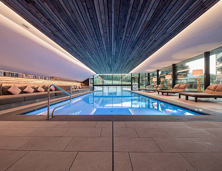 Elegante piscina coperta con lettini moderni e pareti in vetro che offrono vista sulla natura.