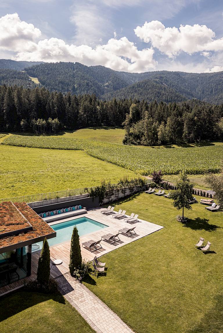 Una moderna casa con piscina in un paesaggio verde, circondata da colline e boschi.