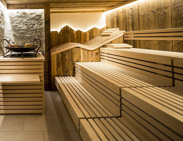 Sauna con rivestimenti in legno e panche a gradini, luce soffusa crea un'atmosfera rilassante.