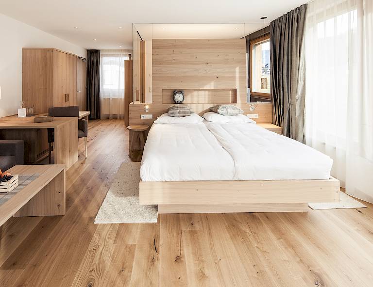 Camera d'albergo moderna e luminosa con mobili in legno, un letto matrimoniale e tonalità naturali. Grandi finestre.