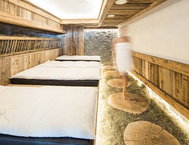 Una stanza in stile benessere con rivestimenti in legno, tre lettini imbottiti e una persona in asciugamano.