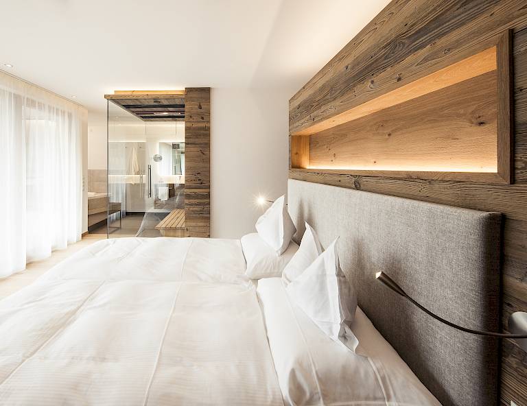 Camera d'albergo moderna con letto matrimoniale, pannelli in legno e grande specchio; luce soffusa.