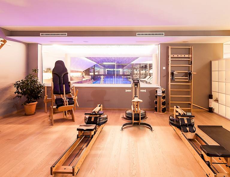Sala fitness con attrezzi in legno e vista su piscina attraverso una grande finestra.