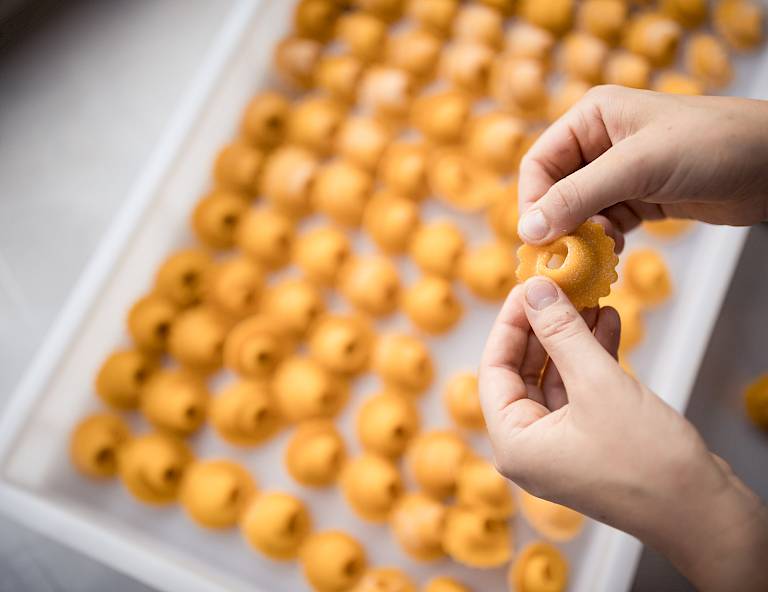 Mani modellano pasta gialla su un vassoio con ravioli crudi.