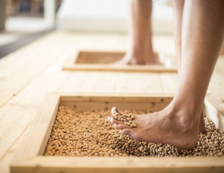 Piedi nudi su una cassa di legno con piccoli ciottoli per massaggio plantare.