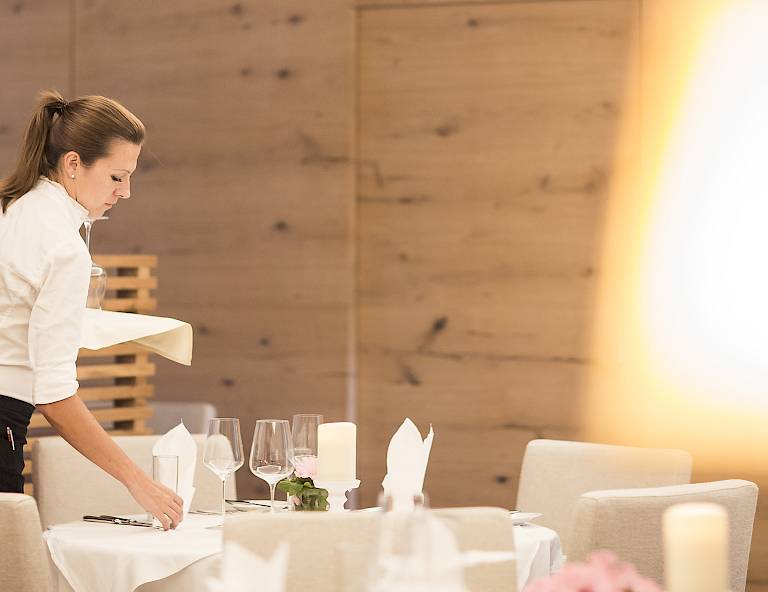 Una cameriera prepara un tavolo elegante con tovaglie bianche in un ristorante.