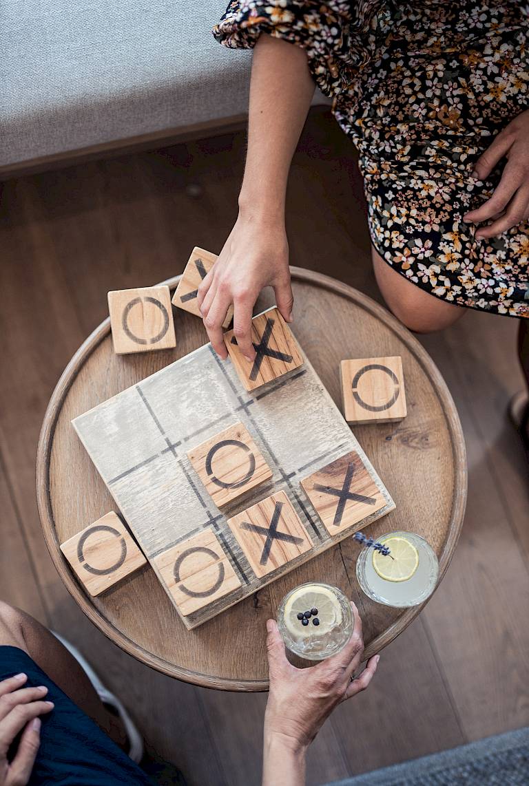 Gioco di tris in legno mentre due persone bevono limonata. Le mani muovono i segnalini.