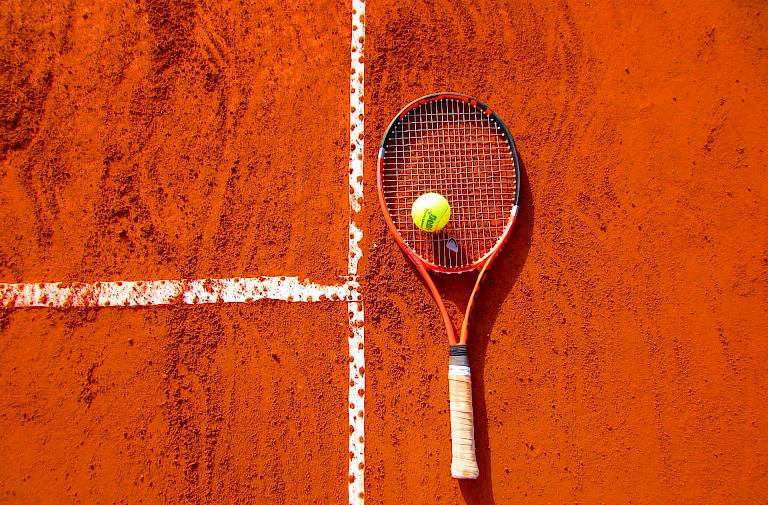 Tennisschläger und Ball auf rotem Sandplatz neben der weißen Linienmarkierung.