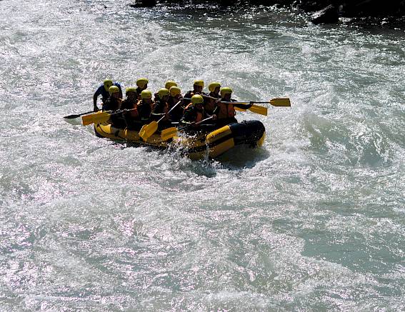 Gruppo impegnato nel rafting su fiume con un gommone giallo in acque rapide.