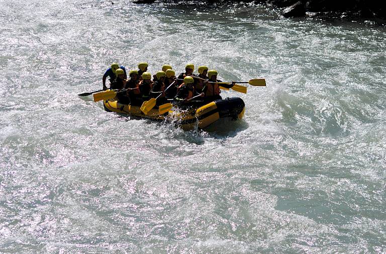 Gruppe beim Wildwasser-Rafting in einem gelben Schlauchboot auf einem schnell fließenden Fluss.