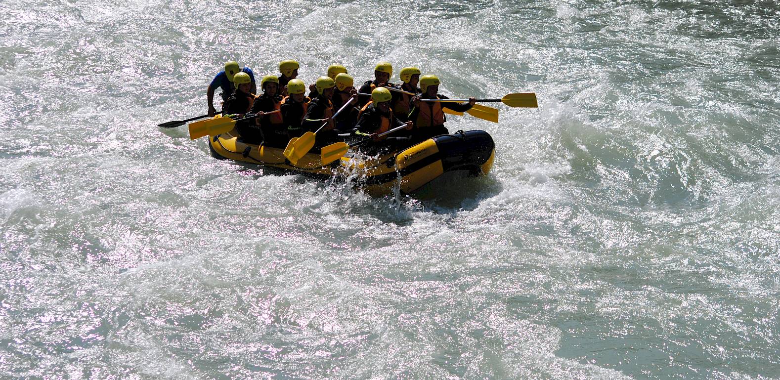 Gruppe von Menschen beim Rafting in einem wilden Fluss, alle tragen gelbe Helme und Schwimmwesten.