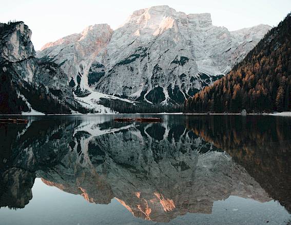 Vista di un lago alpino con chiara riflessione delle montagne innevate sullo sfondo all'alba.