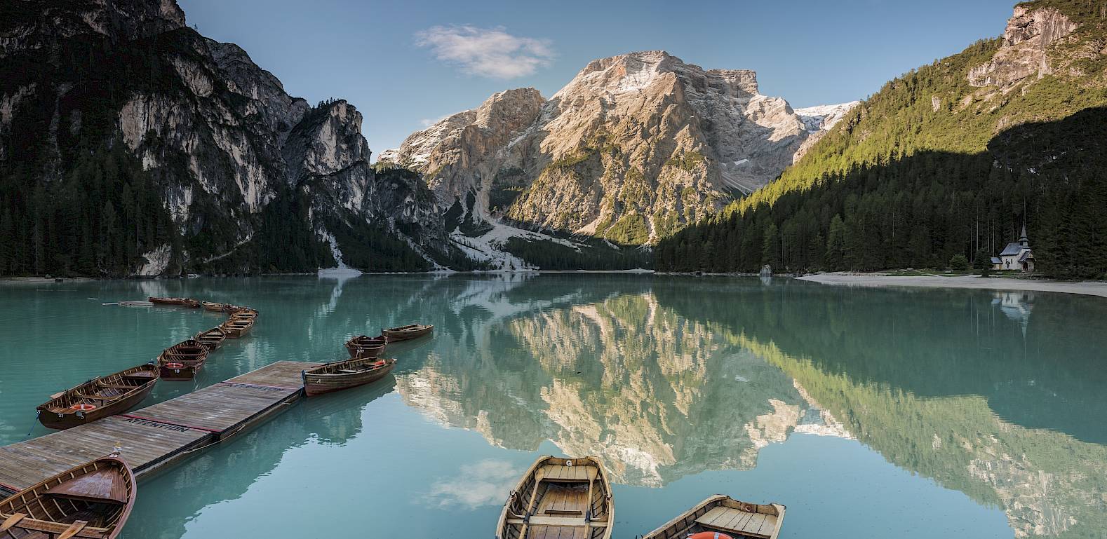 Barche di legno su un lago tranquillo, circondate da montagne imponenti e foreste, riflesse nell'acqua limpida.