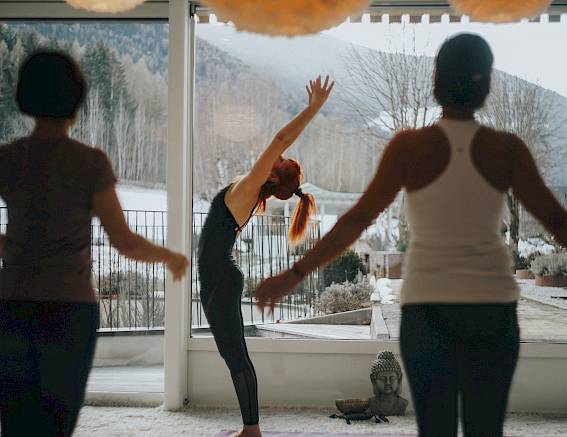 People practicing yoga in a bright room with a view of a snowy landscape and mountains.