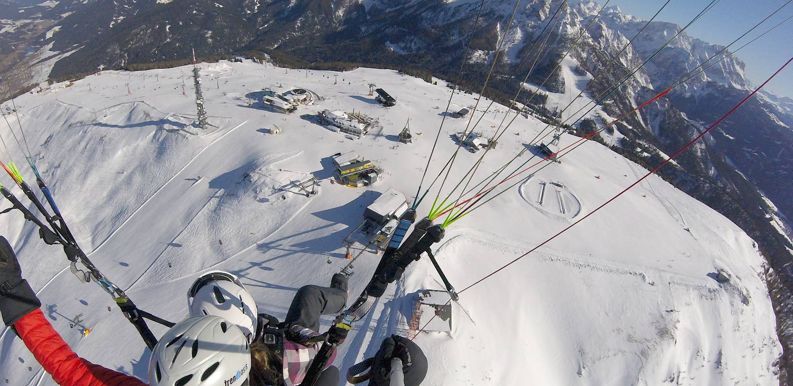 Due persone in parapendio tandem sopra montagne innevate, con cielo limpido e azzurro.