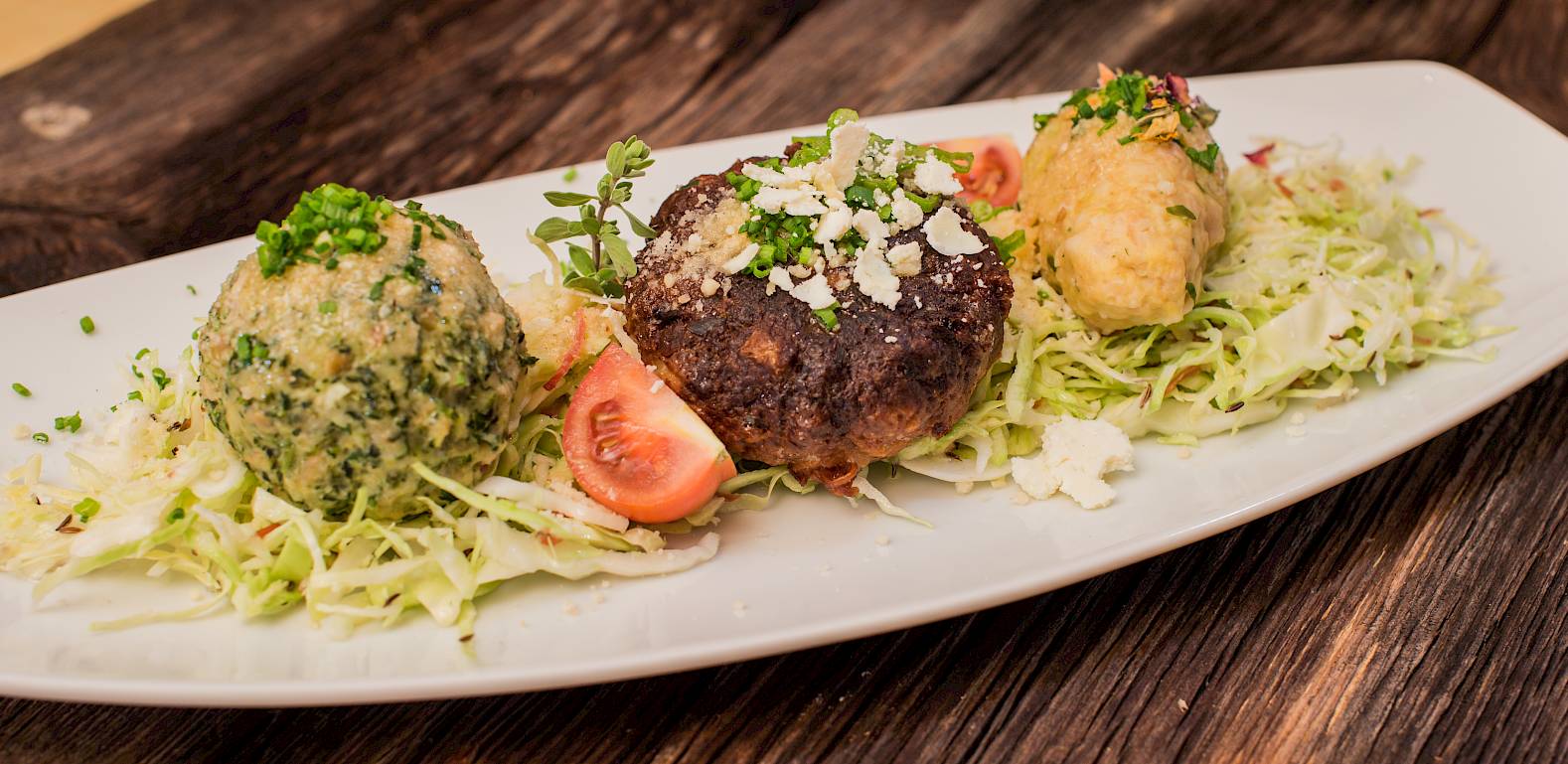 Drei verschieden gewürzte Knödel auf Salatbett, garniert mit Tomaten und Kräutern auf einem weißen Teller.