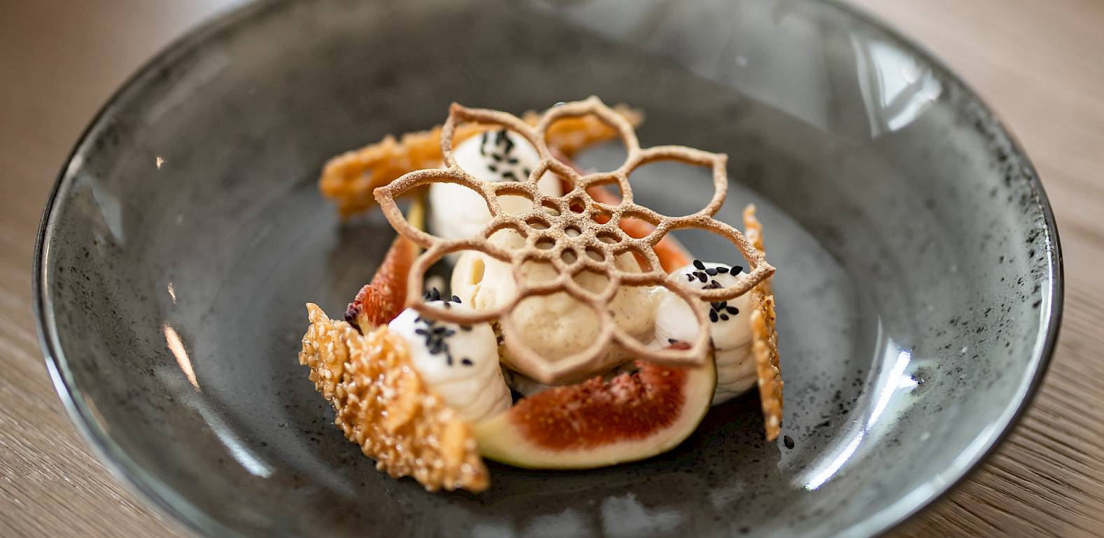 An artfully arranged dessert with fine edible decorations on a grey plate.