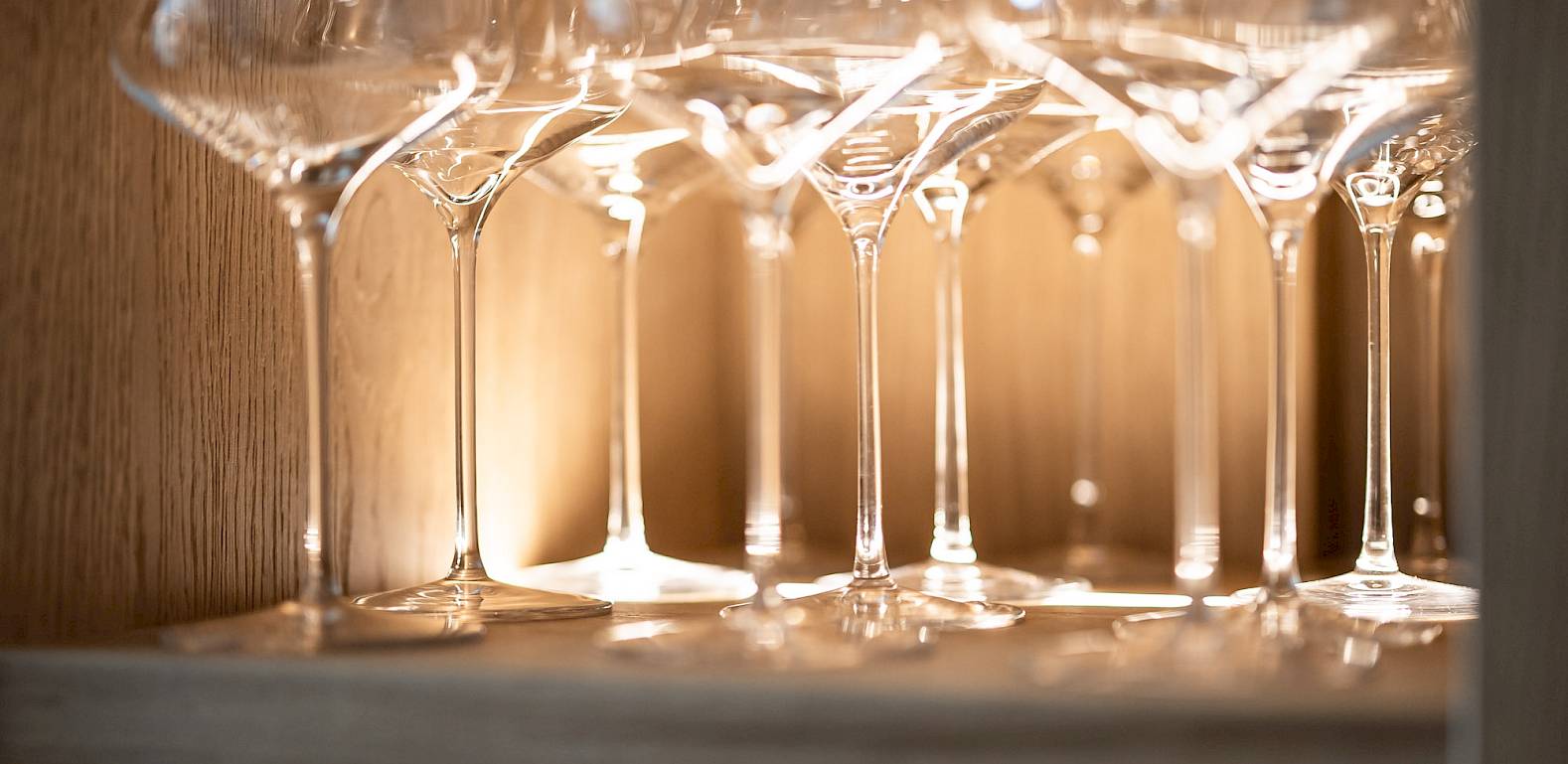 Shelf with elegant wine glasses backlit, appearing shiny and luminous.