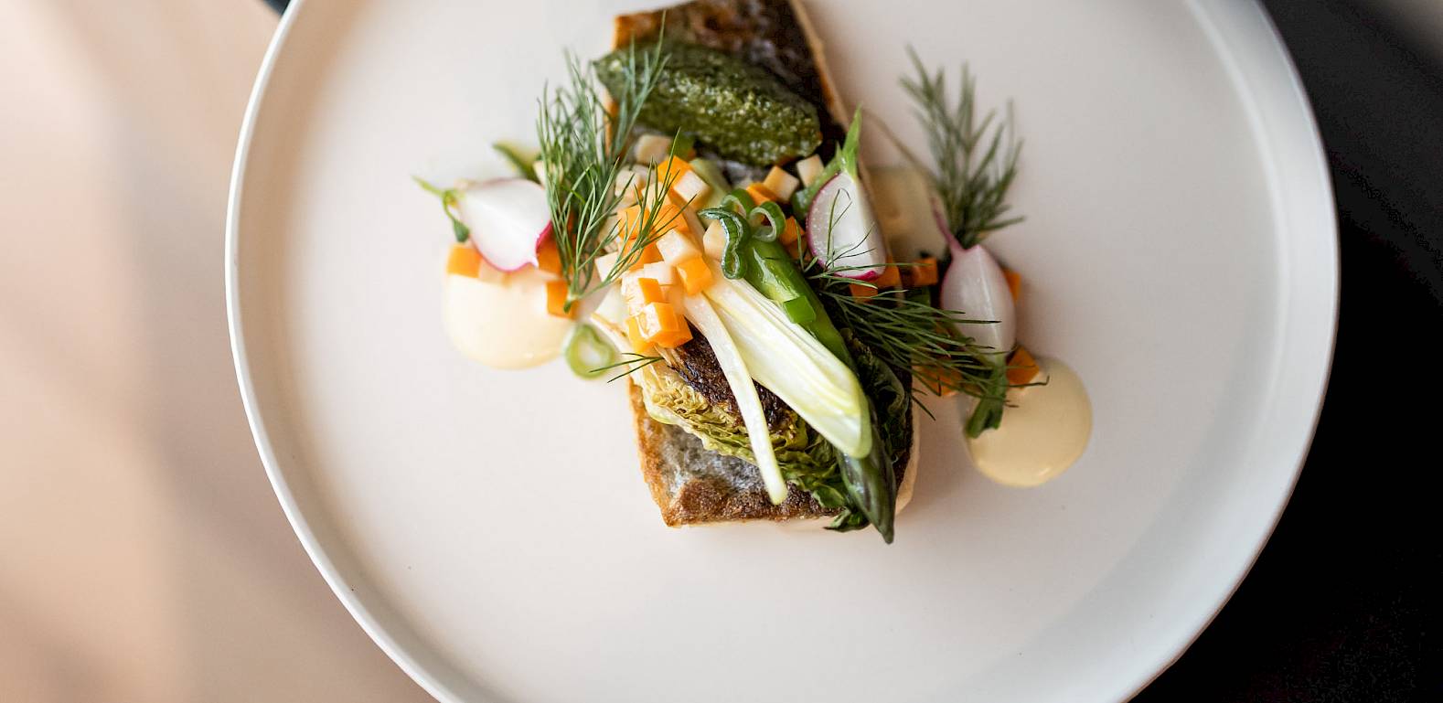 Un piatto di pesce artisticamente disposto su un piatto bianco, guarnito con erbe e verdure.