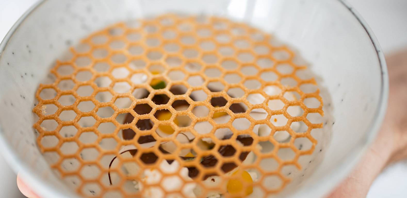 Una mano tiene una ciotola con griglia decorativa di pasta sopra un piatto.