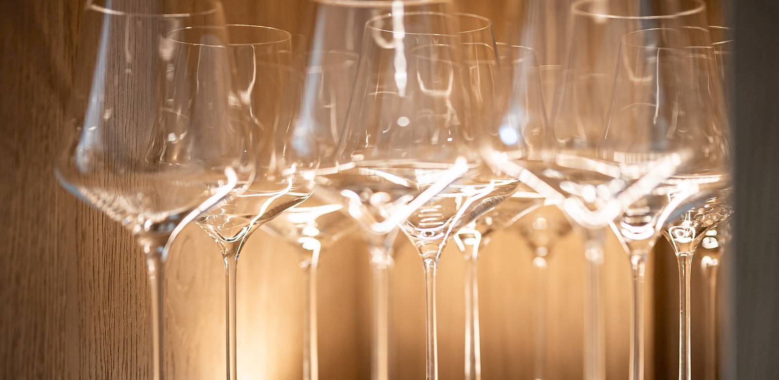 Una mensola di legno con file di eleganti bicchieri da vino, illuminati da una luce calda.