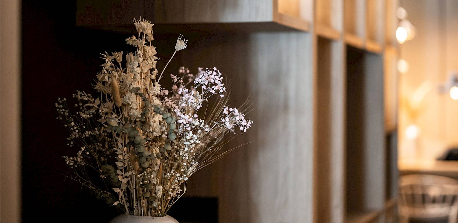 Vaso con fiori secchi su scaffale di legno in un interno moderno con luce soffusa.