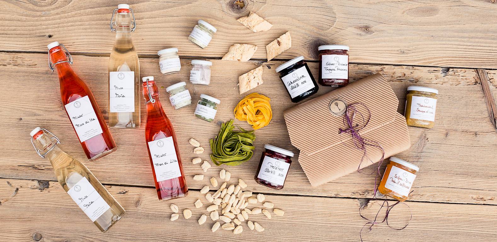 Bottiglie, marmellate e pasta su sfondo di legno, con pacchetto regalo. Varie delizie disposte.