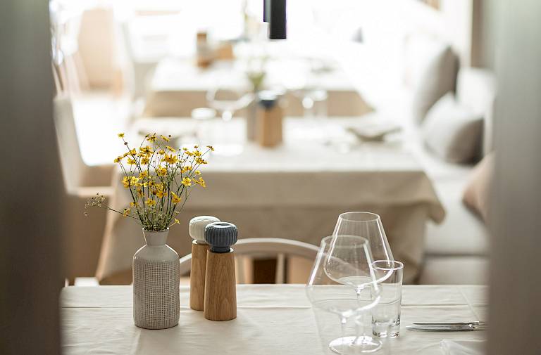Elegantes Restaurant mit gedecktem Tisch, Blumen, Gläsern und Besteck, im Hintergrund weitere Tische.
