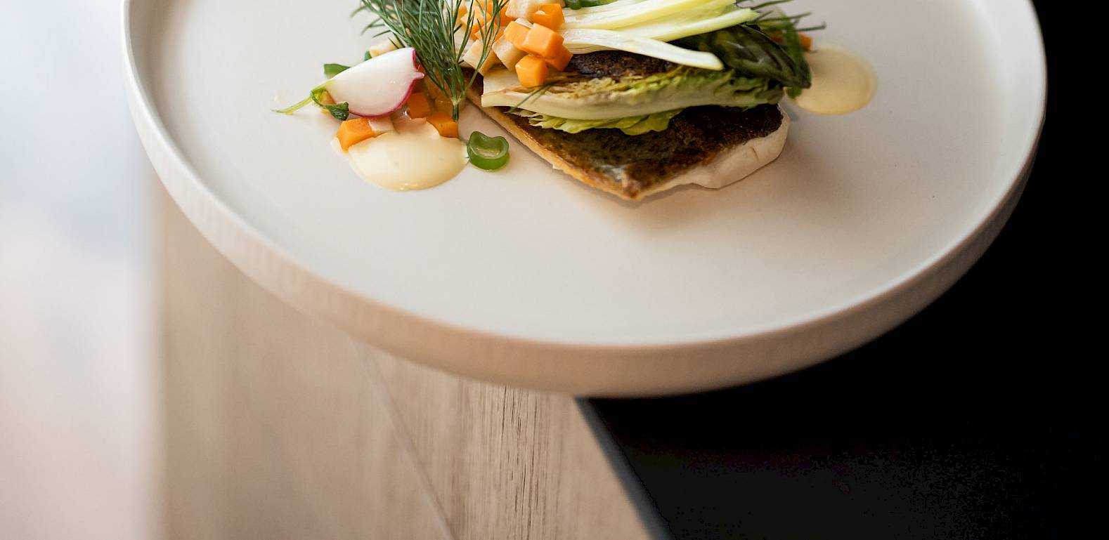 Ein elegantes Gourmetgericht auf einem weißen Teller, kunstvoll mit Gemüse und Kräutern garniert.