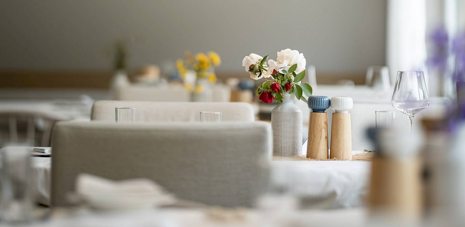 Moderne Restaurant-Innenansicht mit eleganten Hängelampen und gedeckten Tischen, Blumenstrauß in der Mitte.