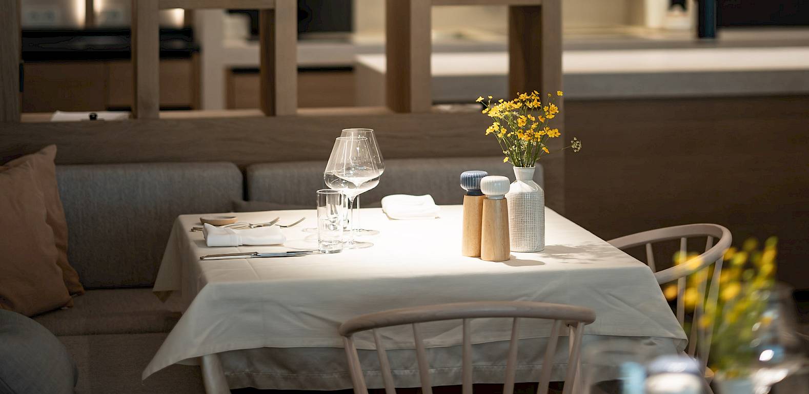 Ein elegantes Restaurant mit Holzregalen, darin bunte Gläser. Zwei gedeckte Tische im Vordergrund.