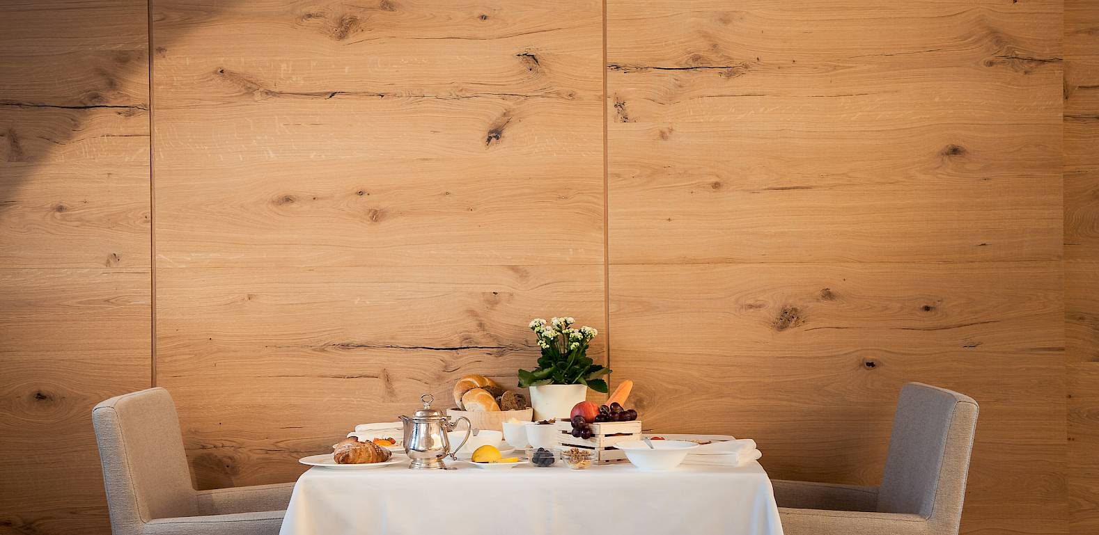 Ein gedeckter Tisch mit Frühstück und Blumen in einem eleganten Raum mit Holzwänden.