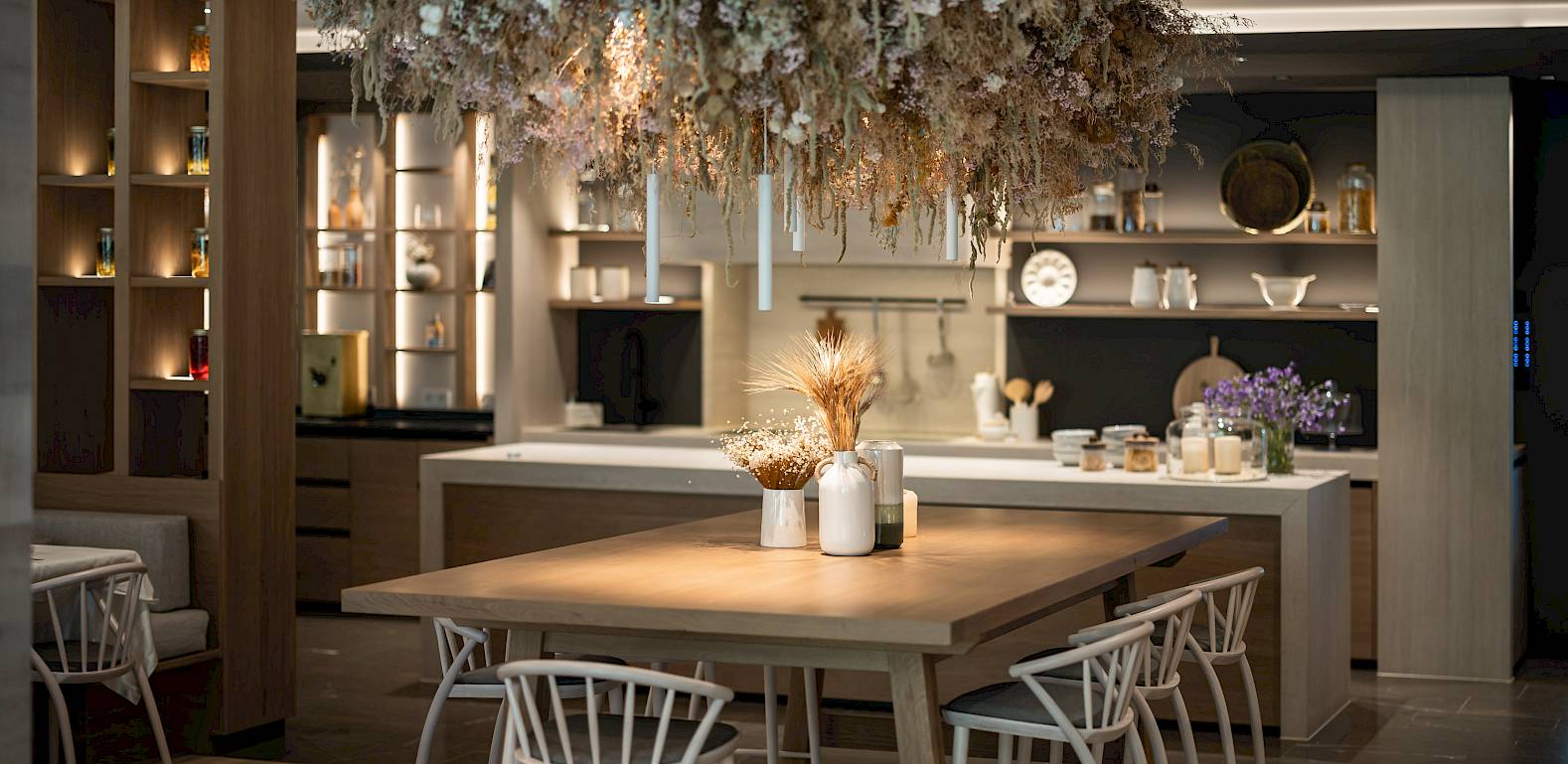 Elegante, moderne Küche mit Holzdetails, heller Dekoration und einem Tisch, umgeben von weißen Stühlen.