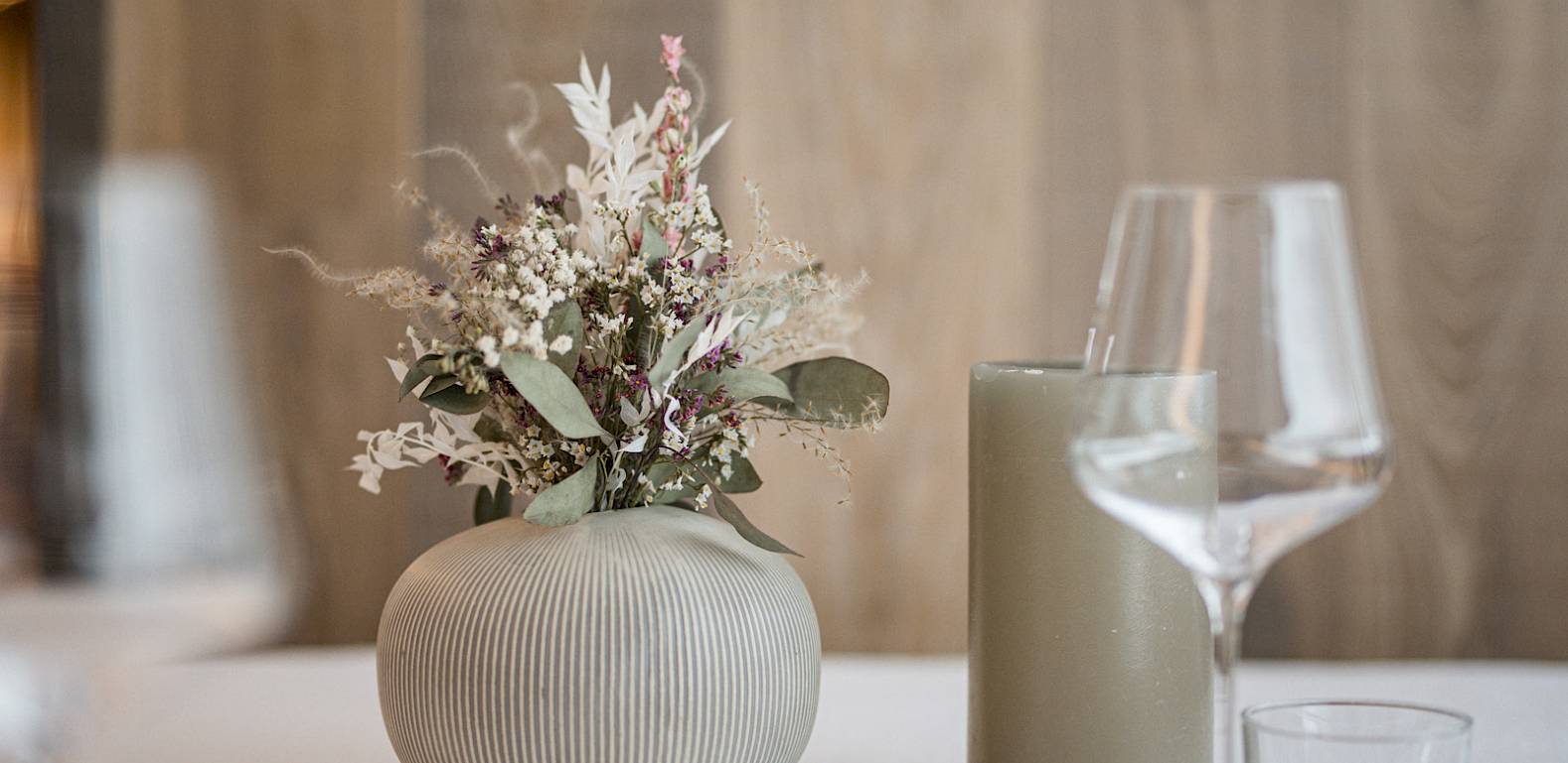 Ein eleganter Tisch mit Blumen in einer Vase, Weingläsern und einem modernen, minimalistischen Dekor.