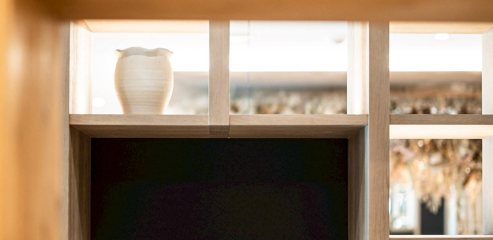 Vase mit Trockenblumen auf einem Regal, darunter eine Holzstruktur. Modern und schlicht dekoriert.